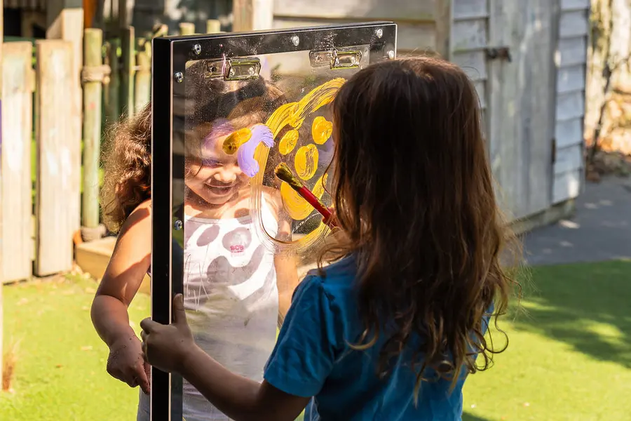 Two children painting together on a double-sided easel